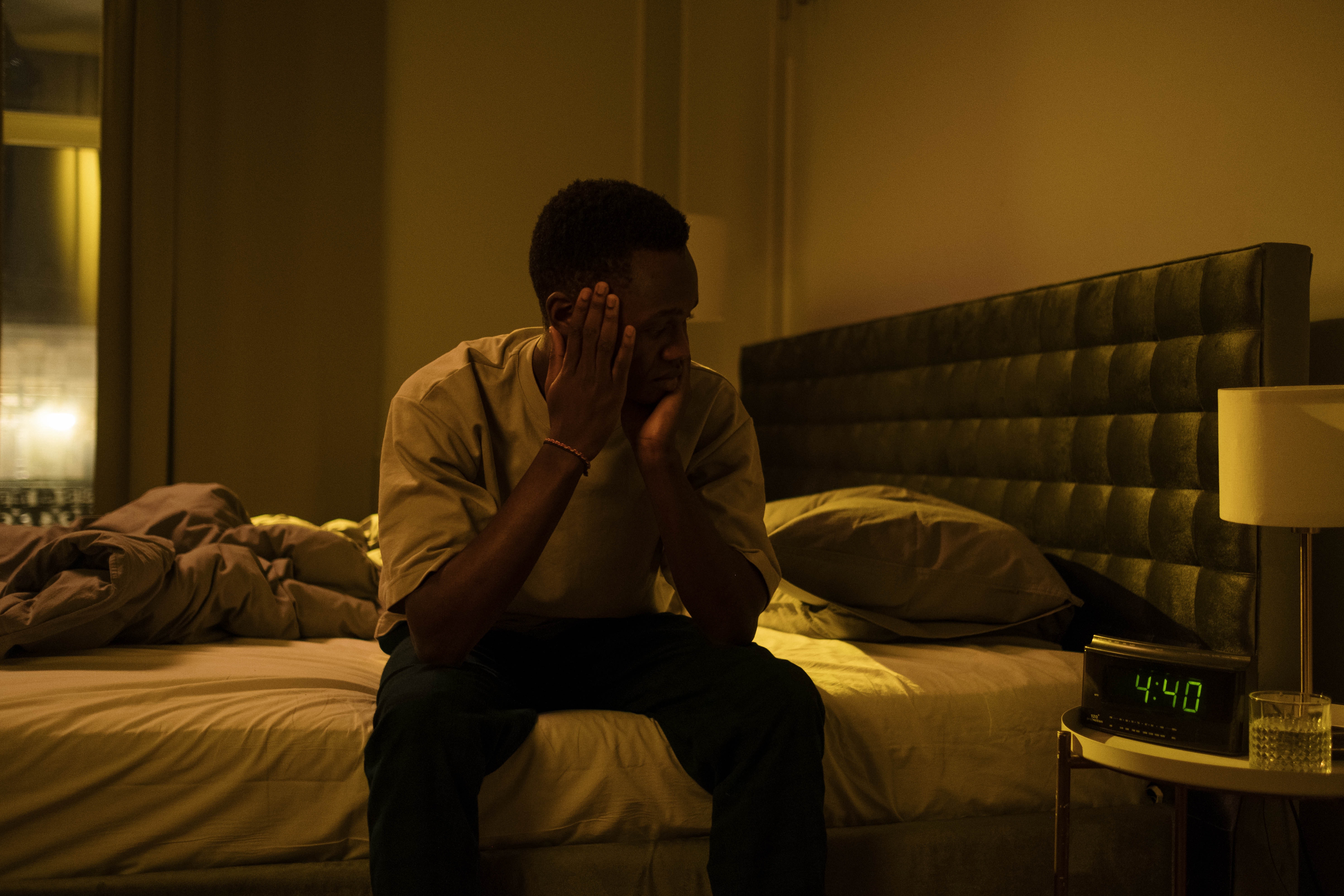 Sleepless man looks at his clock while sitting on his bed